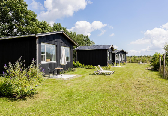 File di tiny house nere con terrazze e sedie sdraio sull’erba a The Kremmer, nei Paesi Bassi.