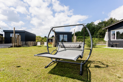 Outdoor lounging space at Tiny House XL at The Kremmer in the Netherlands with a hammock chair on lawn.