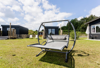 Zona relax esterna al Tiny House XL presso The Kremmer, Paesi Bassi, con sedia amaca su prato verde.