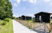 Tiny House XL au Kremmer aux Pays-Bas avec des cabanes en bois noir, une clôture et un sentier verdoyant.