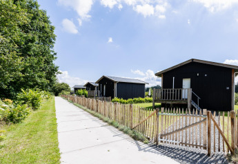 Tiny House XL au Kremmer aux Pays-Bas avec des cabanes en bois noir, une clôture et un sentier verdoyant.