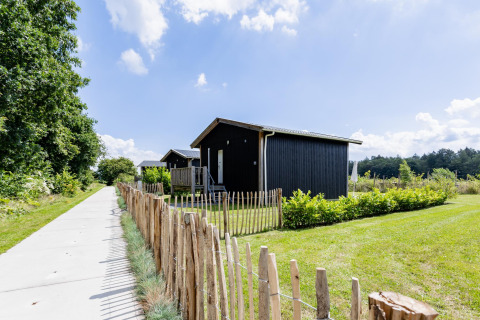 Tiny black house at The Kremmer in the Netherlands, with a wooden fence and green grassy surroundings.