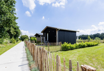 Pequeña casa negra en The Kremmer, Países Bajos, rodeada de césped verde y una valla de madera.
