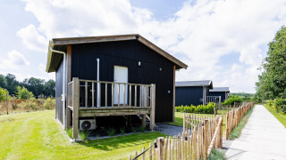 Tiny House XL en The Kremmer, Países Bajos, casa pequeña de madera negra con terraza y jardín vallado.