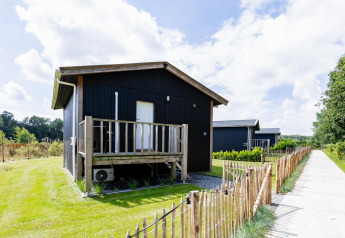 Tiny House XL en The Kremmer, Países Bajos, casa pequeña de madera negra con terraza y jardín vallado.