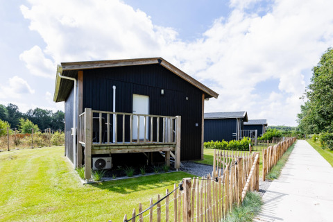 Schwarzes Tiny House XL bei The Kremmer in den Niederlanden mit Terrasse und Holzzaun am Weg.