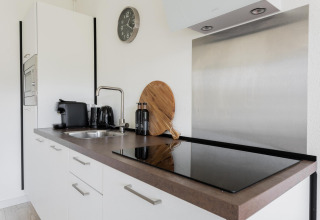 Modernes, kleines Kücheninterieur mit weißem Schrank, Kaffeemaschine und Herdplatte in Tiny House XL.