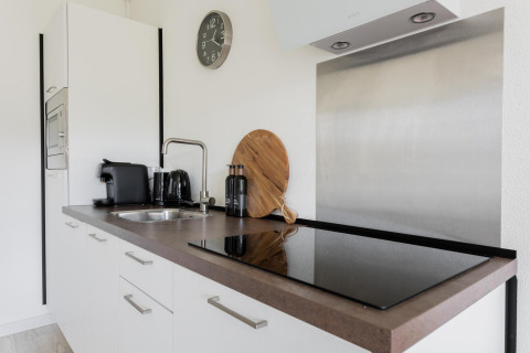 Pequeña cocina moderna con encimera negra, electrodomésticos y gabinetes blancos en Tiny House XL.