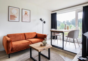 Sala de estar moderna en Tiny House XL en The Kremmer, Países Bajos, con sofá naranja y vista amplia.