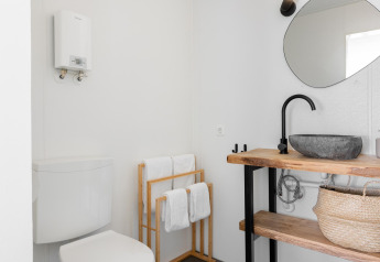 Baño pequeño moderno con estantes de madera, lavabo negro, inodoro y toallas en Tiny House XL, Países Bajos.