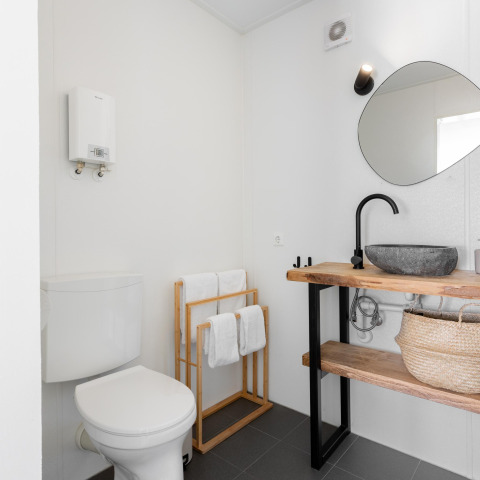 Modernes kleines Badezimmer mit Holzregalen, schwarzem Waschbecken, WC und Handtüchern in Tiny House XL, Niederlande.