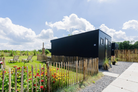 Moderne tiny house met terras en tuin bij The Kremmer in Nederland, omgeven door een houten hek.