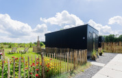 Tiny house moderna con terrazza e giardino a The Kremmer, Paesi Bassi, circondata da una staccionata.