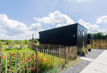 Moderne tiny house med terrasse og blomsterhave på The Kremmer i Holland, omgivet af træhegn.