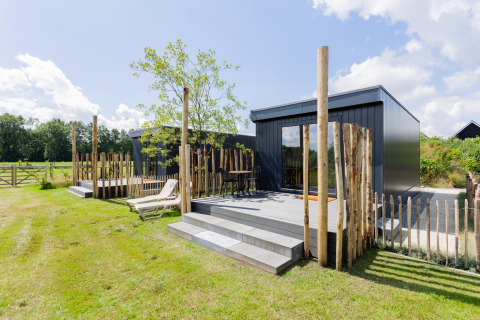 Moderne tiny house met terras en houten omheining, zonnige dag bij The Kremmer in Nederland, groen gazon.