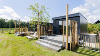 Moderne tiny house med terrasse og træhegn, solrig dag på The Kremmer i Holland, grønne omgivelser.