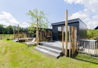 Moderne tiny house met terras en houten omheining, zonnige dag bij The Kremmer in Nederland, groen gazon.