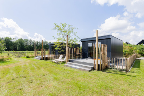 Zwei moderne Tiny Houses mit Holzterrasse bei The Kremmer, Niederlande, auf einer grünen Wiese.