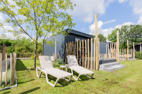 Dos tumbonas frente a una tiny house con terraza en The Kremmer, Países Bajos, rodeada de vegetación.