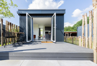 Tiny house met terras en open deuren bij The Kremmer in Nederland, omheind door houten palen.