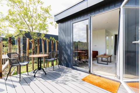 Terraza soleada con dos sillas y mesa junto a un Tiny House con tarima en The Kremmer, Países Bajos.