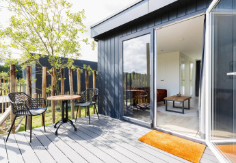Terraza soleada con dos sillas y mesa junto a un Tiny House con tarima en The Kremmer, Países Bajos.