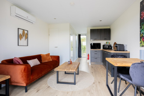 Wohnbereich und Küche im Tiny House mit moderner Einrichtung, Holztisch und orangefarbenem Sofa.