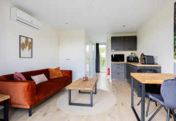 Stue og køkkenområde i Tiny House med moderne indretning, træbord og orange sofa på The Kremmer.