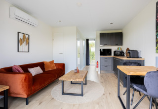 Wohnbereich und Küche im Tiny House mit moderner Einrichtung, Holztisch und orangefarbenem Sofa.