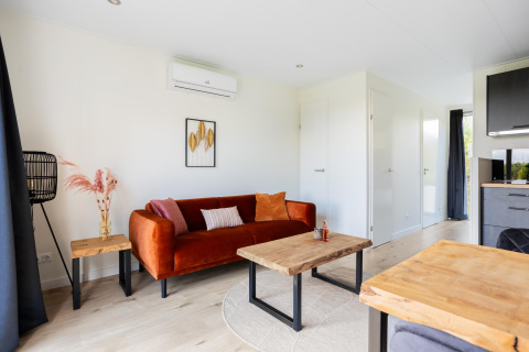 Sala luminosa y moderna de tiny house con sofá naranja y mesas de madera en The Kremmer, Países Bajos.