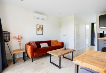 Lyst og moderne tiny house stue med orange sofa, træborde og vægkunst ved The Kremmer, Holland.