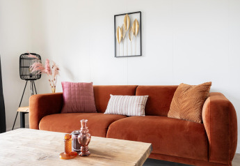 Soggiorno moderno con divano ruggine, cuscini, tavolino e arte da parete nel Tiny House Kremmer.