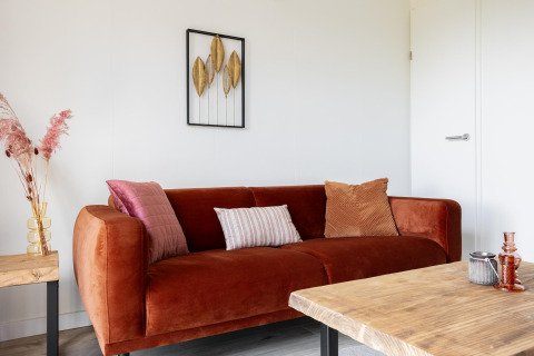 Gemütliches Wohnzimmer im Tiny House mit rostfarbener Sofa, Kissen, Holztisch und Wanddeko bei The Kremmer.