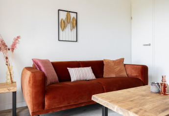 Acogedora sala en Tiny House en The Kremmer, Países Bajos, con sofá naranja, arte y mesa de madera.