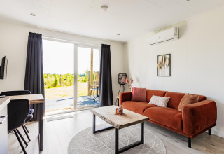 Lichte tiny house woonkamer met oranje bank, houten tafel en tuinuitzicht bij The Kremmer, Nederland.