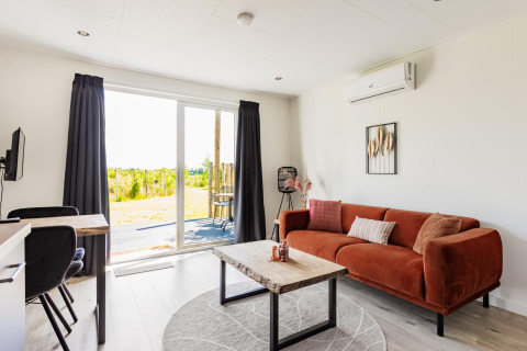 Bright tiny house living room with orange sofa, wood table, and garden view at The Kremmer, Netherlands.
