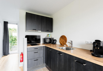 Angolo cottura moderno in una Tiny House a The Kremmer, Paesi Bassi, con mobili scuri e macchina da caffè.