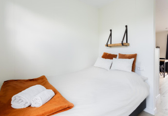 Camera luminosa in tiny house con letto matrimoniale, coperta arancione e asciugamani a The Kremmer, Paesi Bassi.