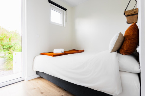 Dormitorio pequeño moderno con cama individual, ropa de cama blanca y ventana grande en Tiny House The Kremmer.