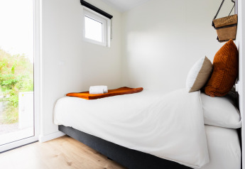 Moderna camera da letto piccola con letto singolo, lenzuola bianche e grande finestra a Tiny House The Kremmer.