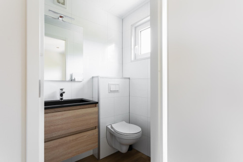 Moderne, kompakt badeværelse med væghængt toilet, vask, spejl og vindue i et tiny house i Holland.