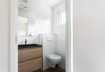 Bagno moderno e compatto con WC sospeso, lavabo, specchio e finestra in una tiny house nei Paesi Bassi.