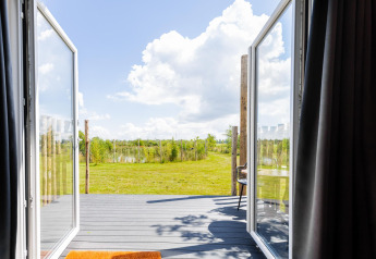Vista da una tiny house sulla terrazza e il prato verde a The Kremmer, Paesi Bassi, in una giornata di sole.