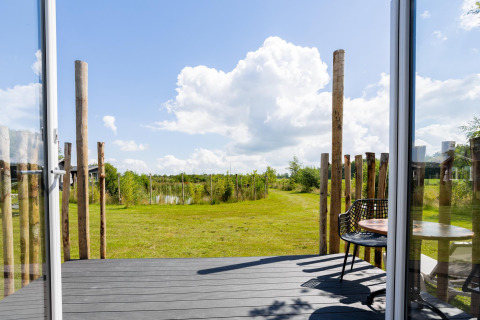 Vista desde una tiny house con terraza en The Kremmer, Países Bajos; puertas abiertas a un jardín verde.