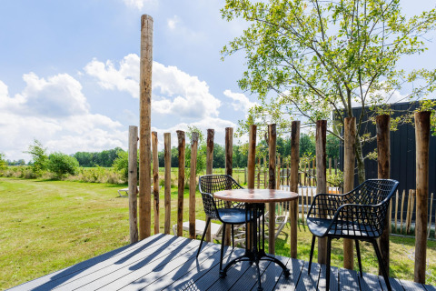 Terraza exterior de una Tiny House con postes de madera, mesa, sillas y vistas al campo en los Países Bajos.