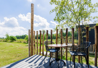 Buitenterras bij een tiny house met houten omheining, tafel, stoelen en zicht op het groen in Nederland.