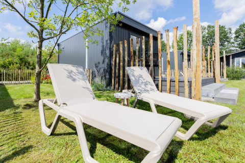 Twee ligstoelen op het gras voor een tiny house met terras en houten palen bij The Kremmer in Nederland
