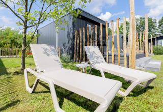 Twee ligstoelen op het gras voor een tiny house met terras en houten palen bij The Kremmer in Nederland