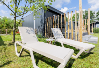 Two lounge chairs on grass outside a tiny house with deck and wooden posts at The Kremmer, Netherlands