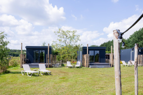 Tiny houses met terrassen en ligstoelen op het gras bij The Kremmer in Nederland op een zonnige dag.